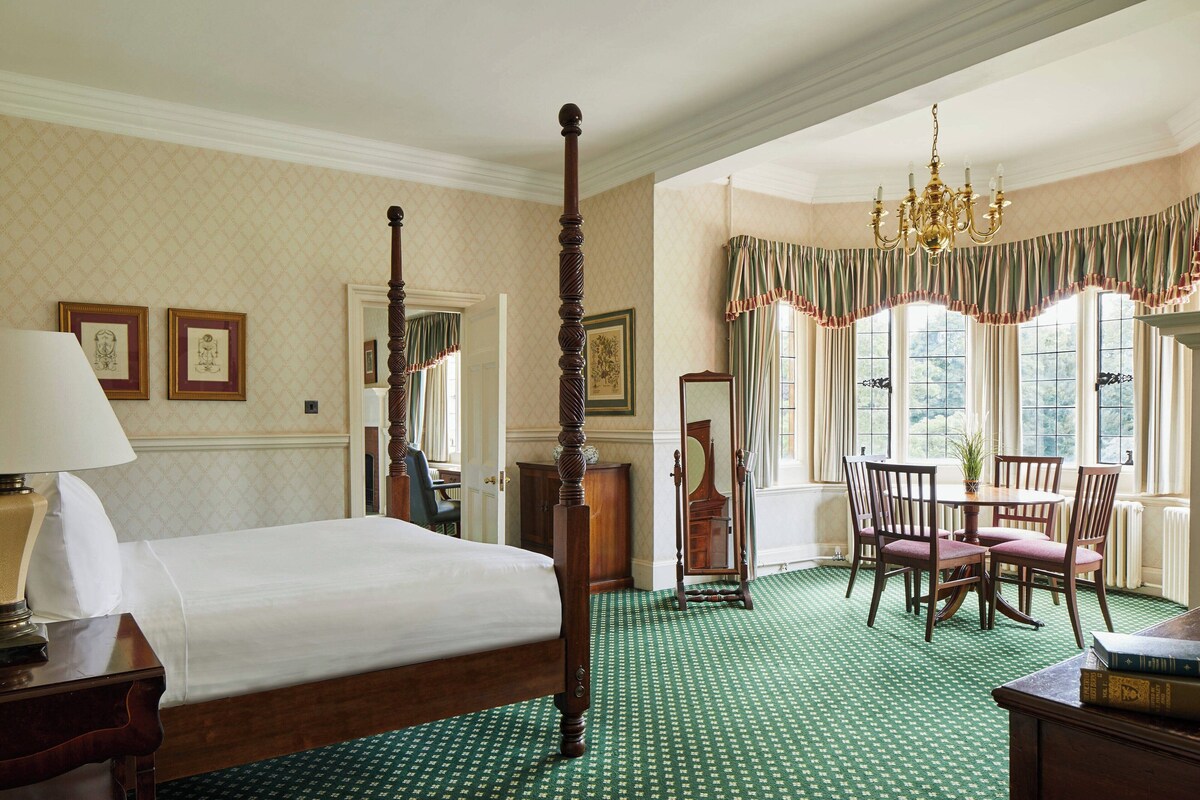 A bedroom with a four-poster bed, a dining table with chairs, and a chandelier.