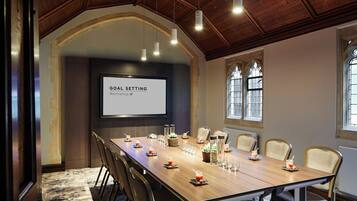 A conference room with a long table, chairs, a projector screen, and a wooden ceiling.