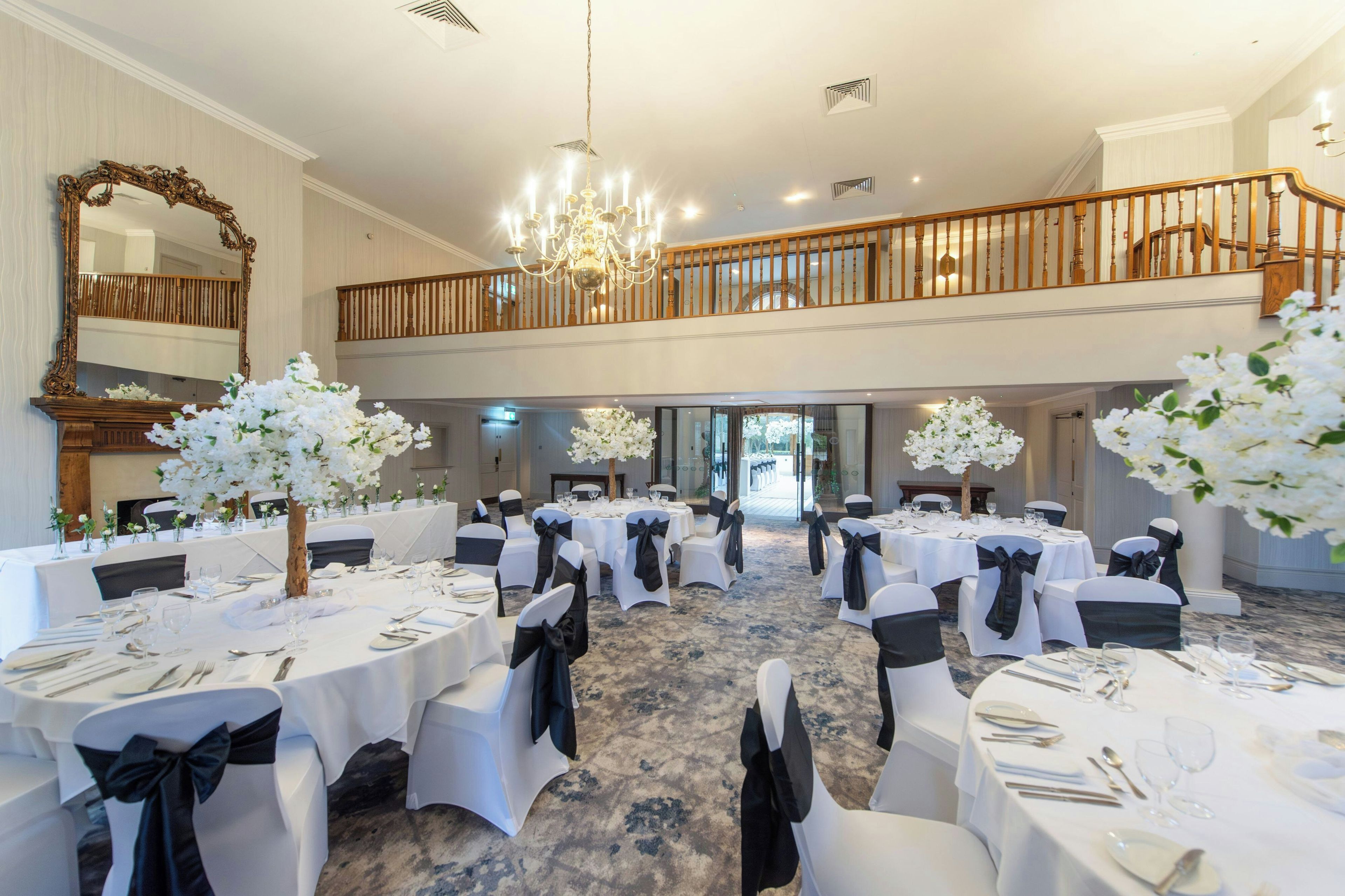 Un salón de banquetes con varias mesas redondas, manteles blancos y cintas negras en las sillas.