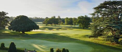 A golf course with well-manicured grass, sand bunkers, and a variety of trees.