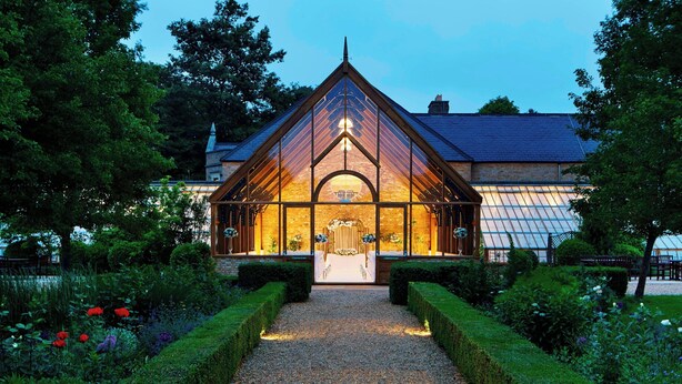 A building with a triangular roof and a central archway, surrounded by well-manicured hedges and a gravel path leading to the entrance. - Hanbury Manor Marriott Hotel & Country Club (Ware)