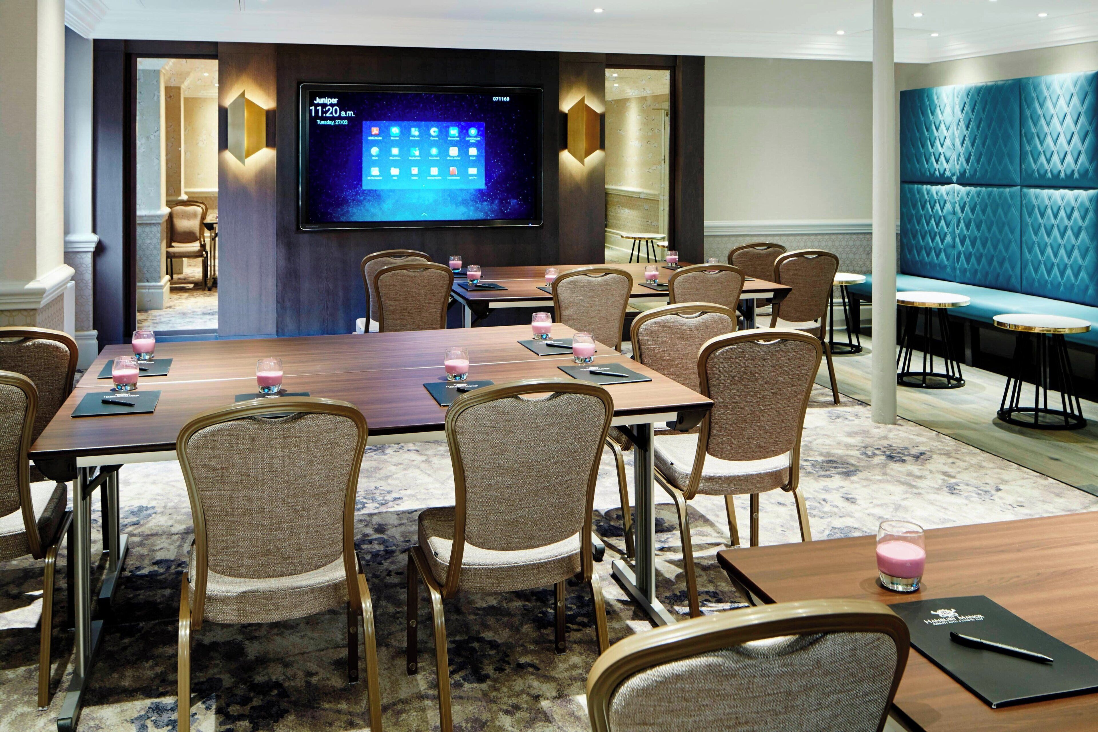 A conference room with a large table, multiple chairs, a TV screen, and a seating area with cushioned benches.