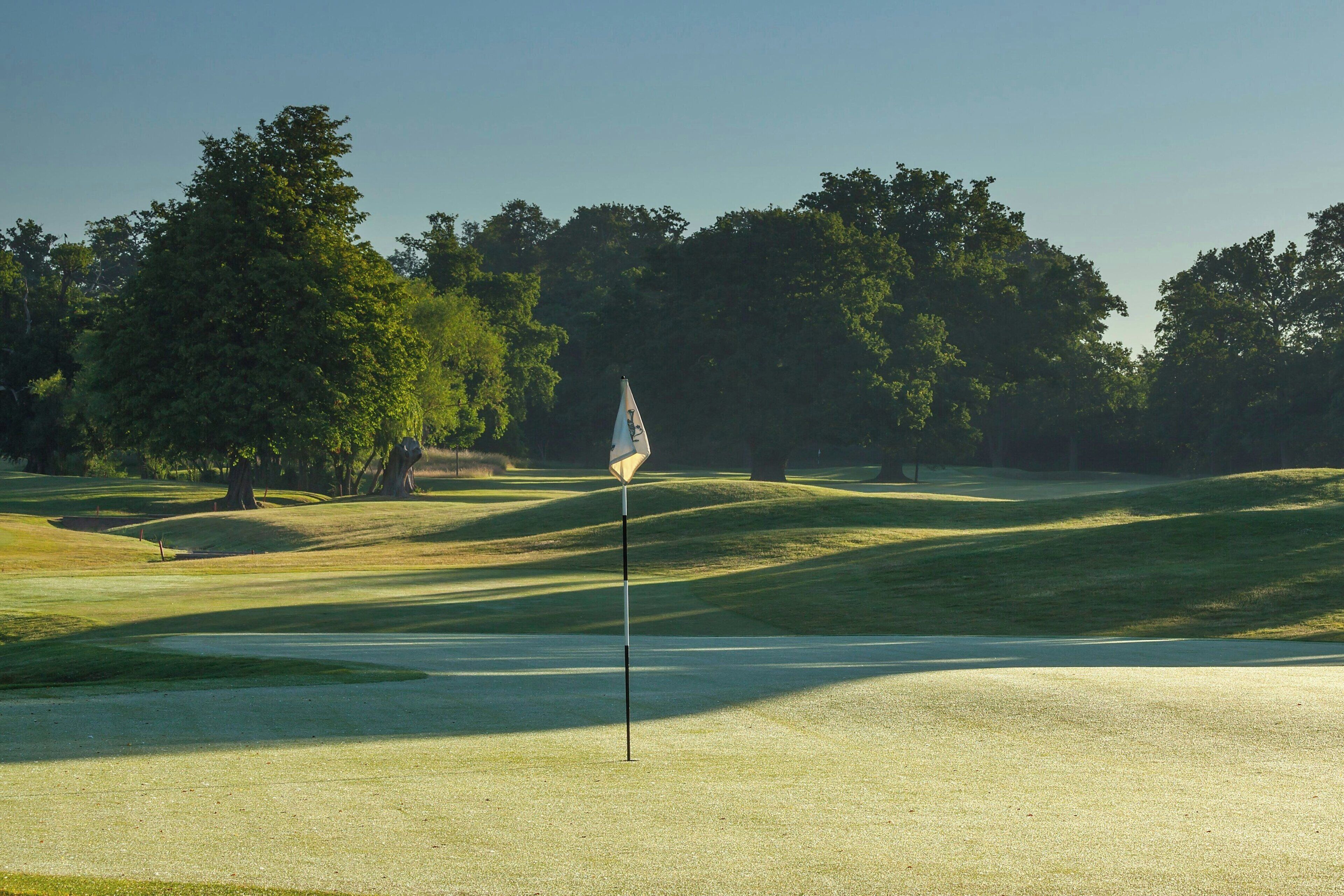 A golf course with a flagstick in the foreground, surrounded by well-manicured grass and trees.