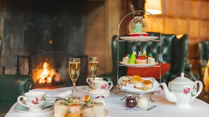 A table set for a tea service with a tiered dessert display, two glasses of champagne, and a teapot. - Hanbury Manor Marriott Hotel & Country Club (Ware)