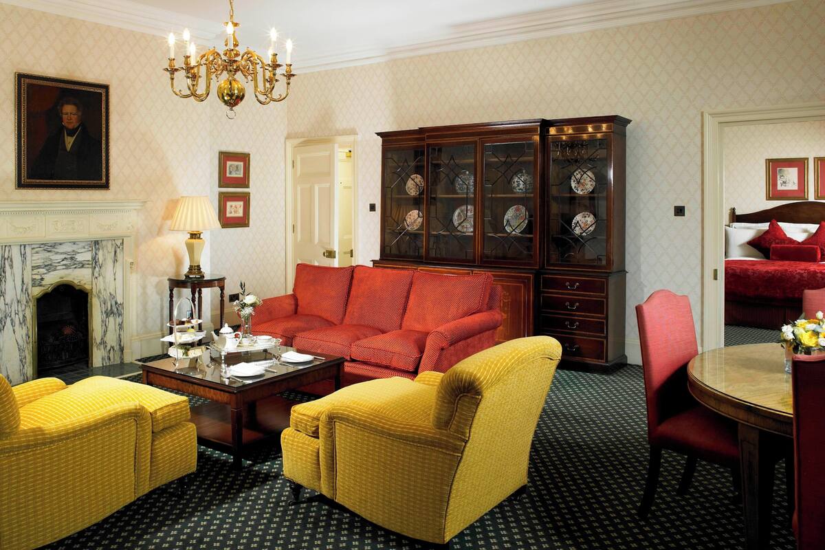 A traditional room with a fireplace, a red sofa, yellow chairs, a wooden cabinet with glass doors, and a dining table with chairs.