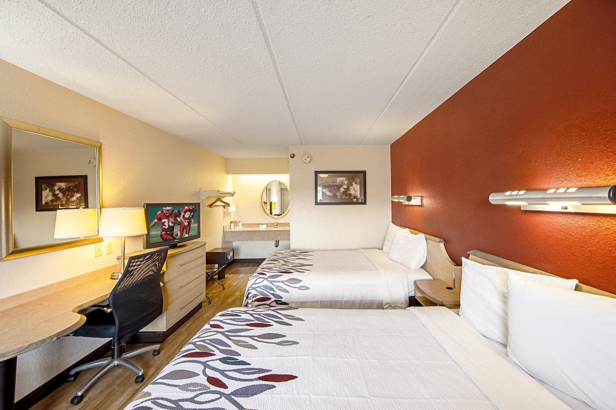 A hotel room with two beds, a desk, a chair, a TV, and a mirror.