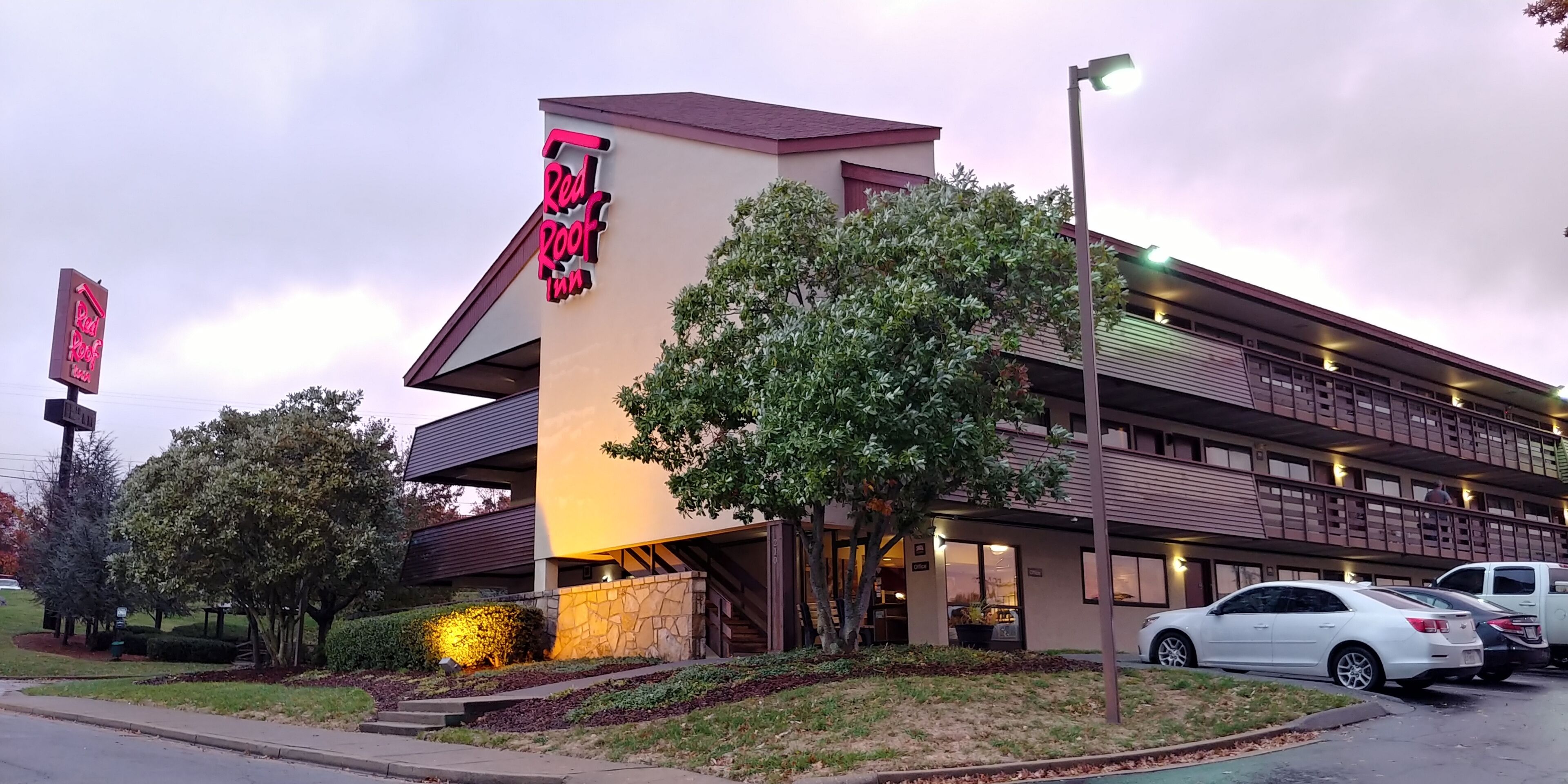 A Red Roof Inn with a modern design, featuring a prominent neon sign, a parking lot, and a well-maintained lawn.