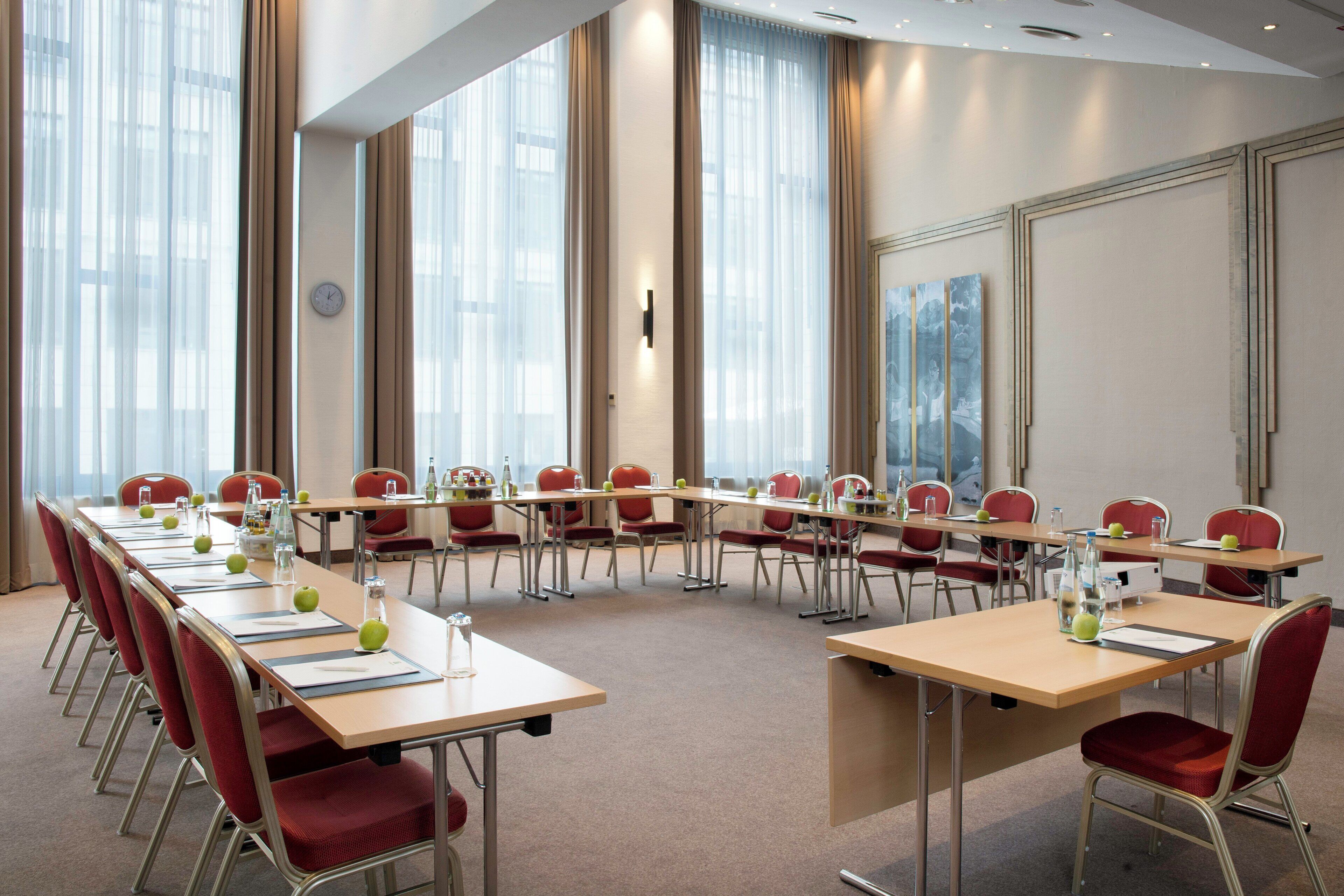 Ein Konferenzraum mit einem langen Tisch, roten Stühlen und einer Uhr an der Wand.