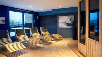 A spa room with wooden loungers, a large window with a view, and a wall-mounted clock.