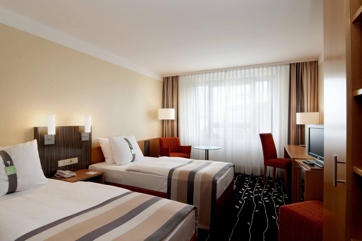 A hotel room with two beds, a desk, a chair, a TV, and a small table.