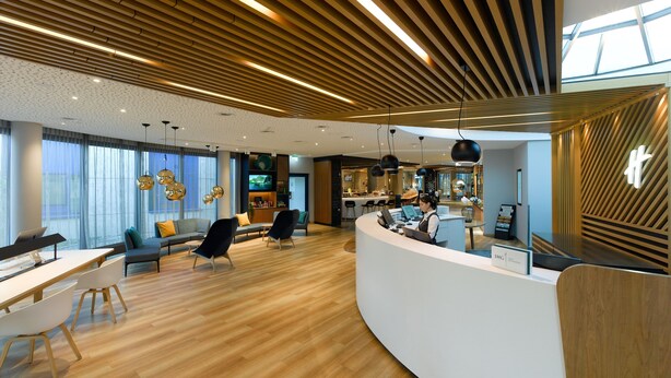 A modern hotel lobby with a curved reception desk, seating area, and a bar. - Holiday Inn Stuttgart by IHG (Stuttgart)