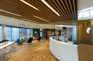 A modern hotel lobby with a curved reception desk, seating area, and a bar.
