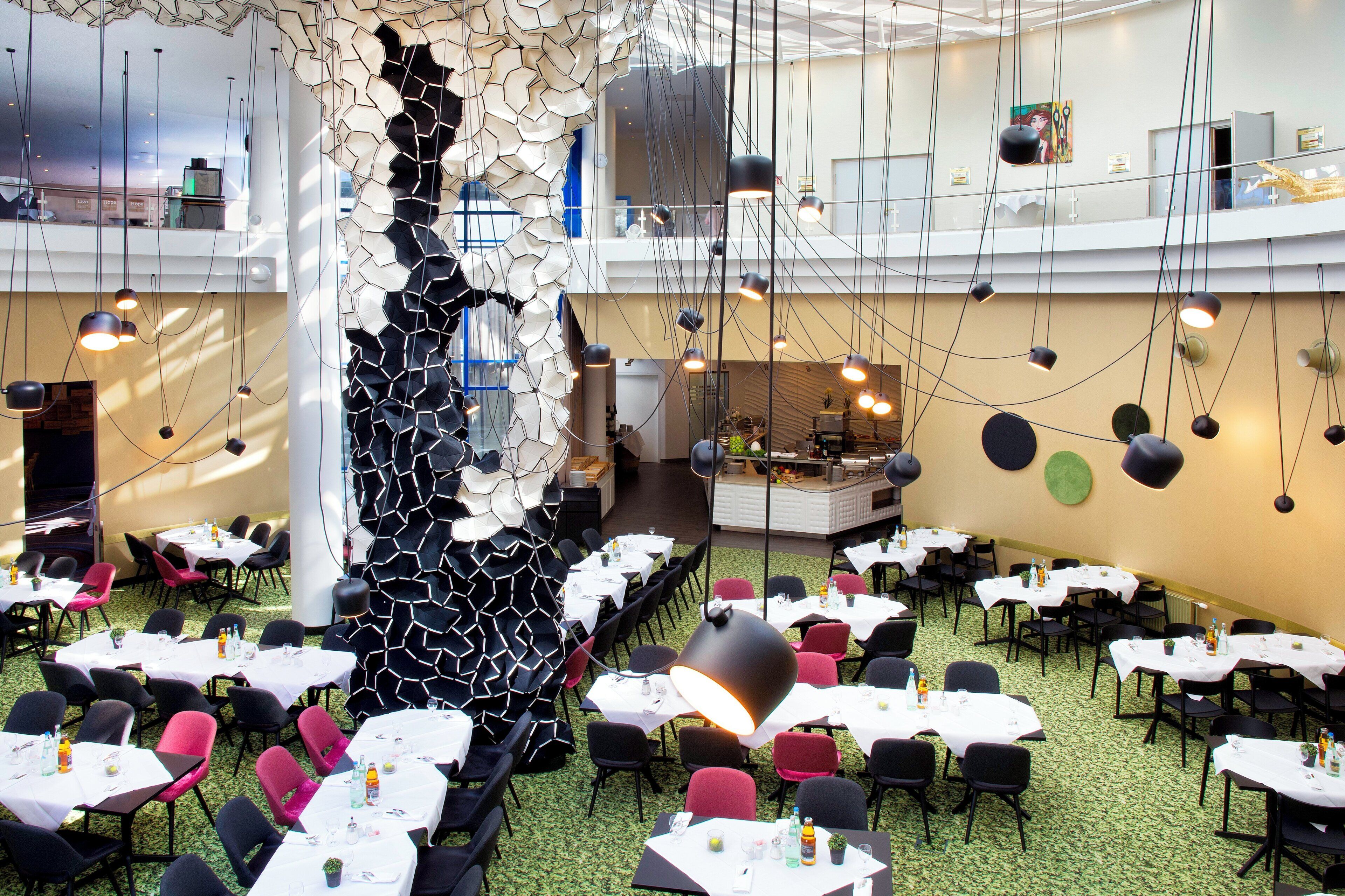 A restaurant with multiple dining tables and chairs, a central decorative wall, and hanging pendant lights.