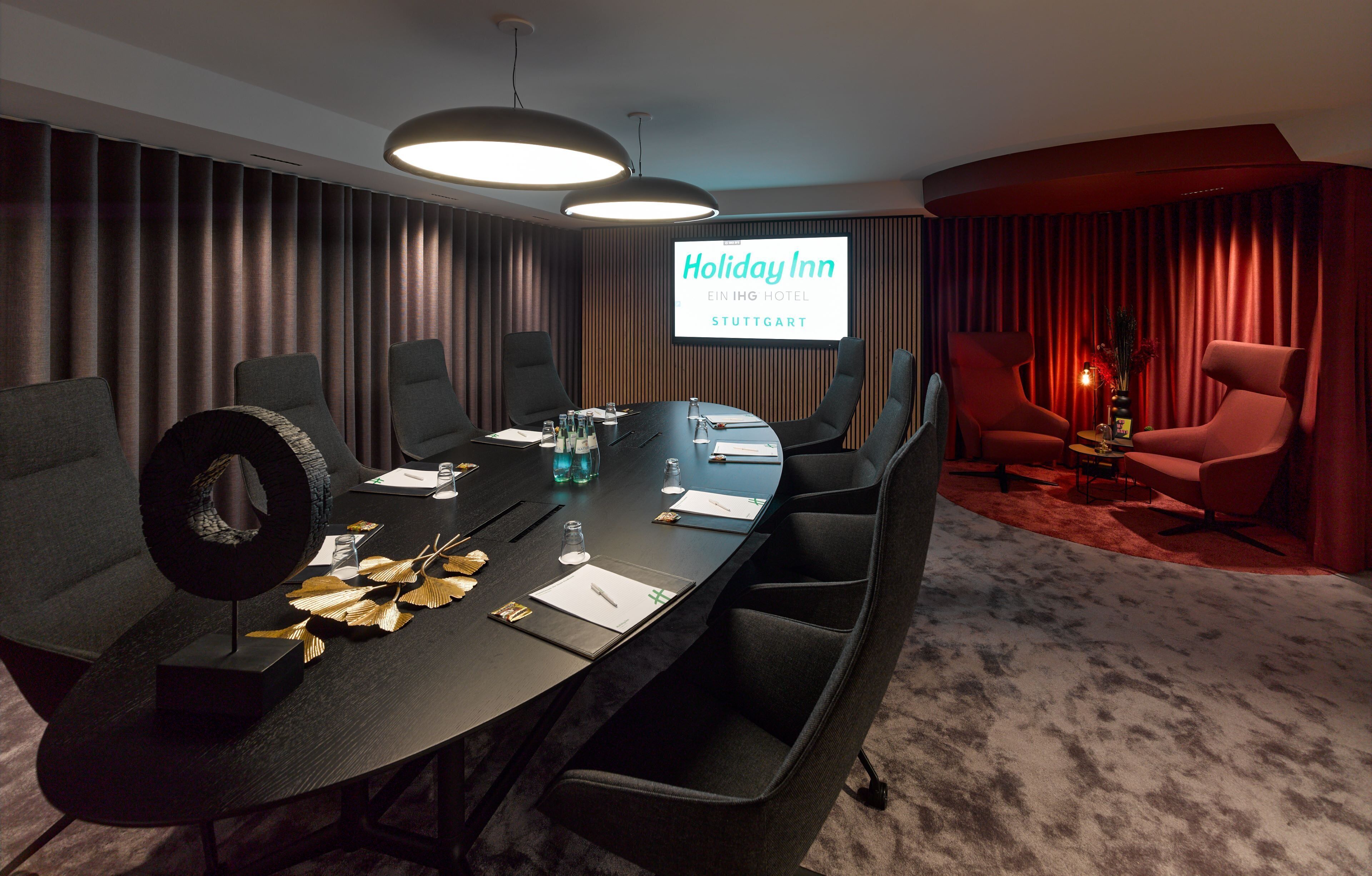 A conference room with a large table, chairs, a projector screen, and a red curtain backdrop.