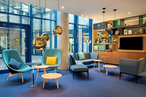 A modern lounge area with seating, a television, and a large window. - Holiday Inn Stuttgart by IHG (Stuttgart)
