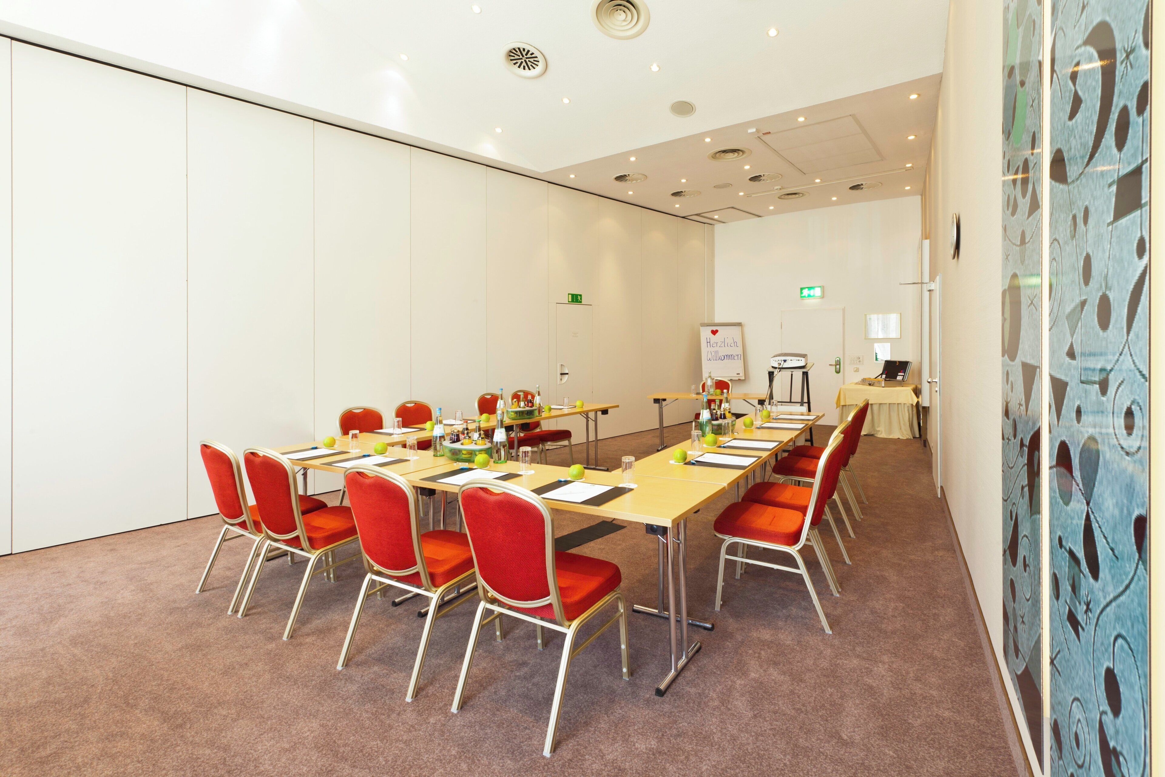 A conference room with a long table, red chairs, and a whiteboard.
