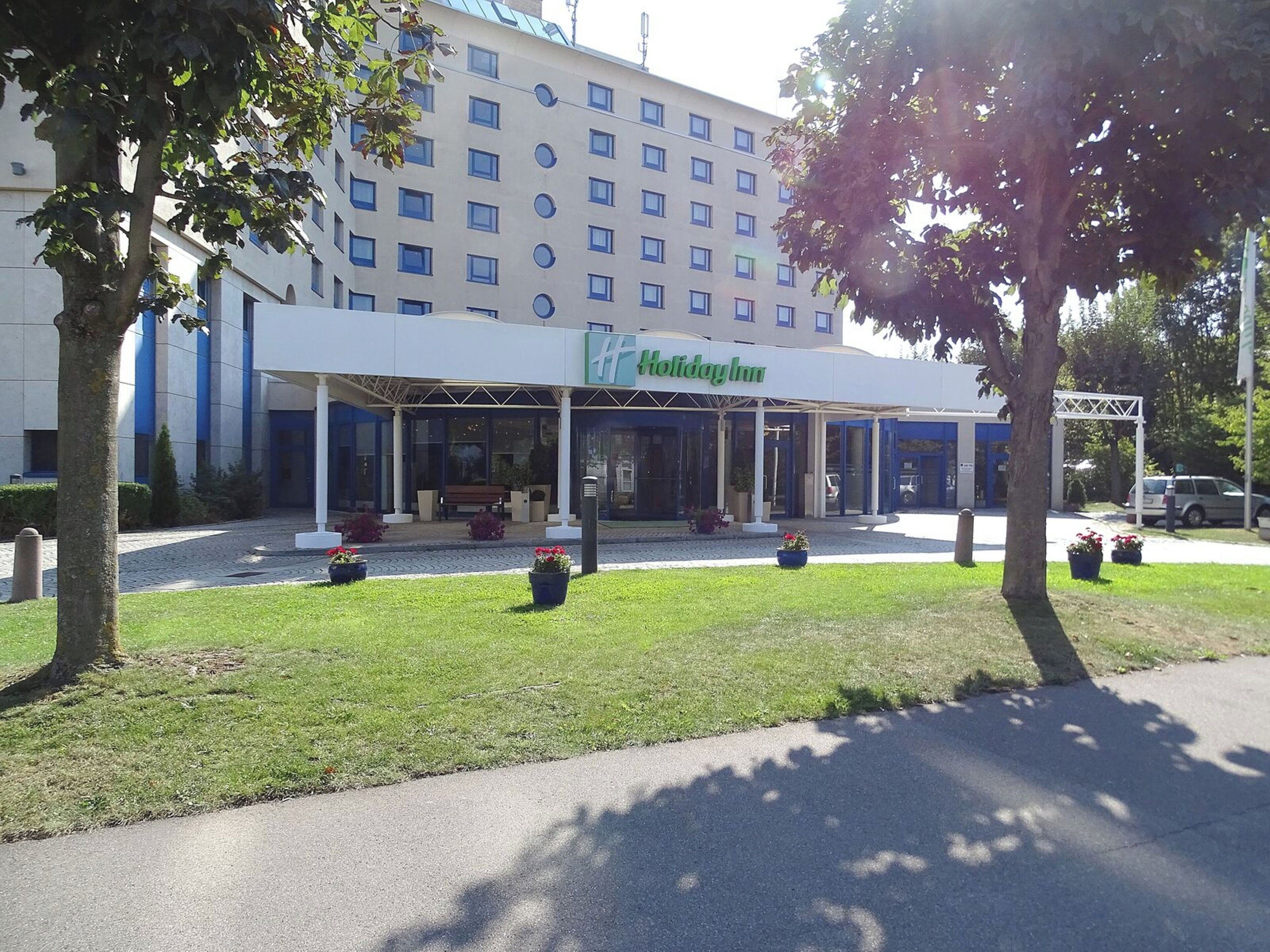 Un hotel Holiday Inn con ingresso coperto, numerose finestre e un'area di parcheggio con piante in vaso.