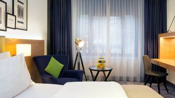 Una camera d'albergo con un letto, una scrivania, una sedia, un tavolino con della frutta e tende.