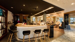 A modern bar area with a white tiled counter, black bar stools, and a seating area with tables and chairs. - Holiday Inn Stuttgart by IHG (Stuttgart)
