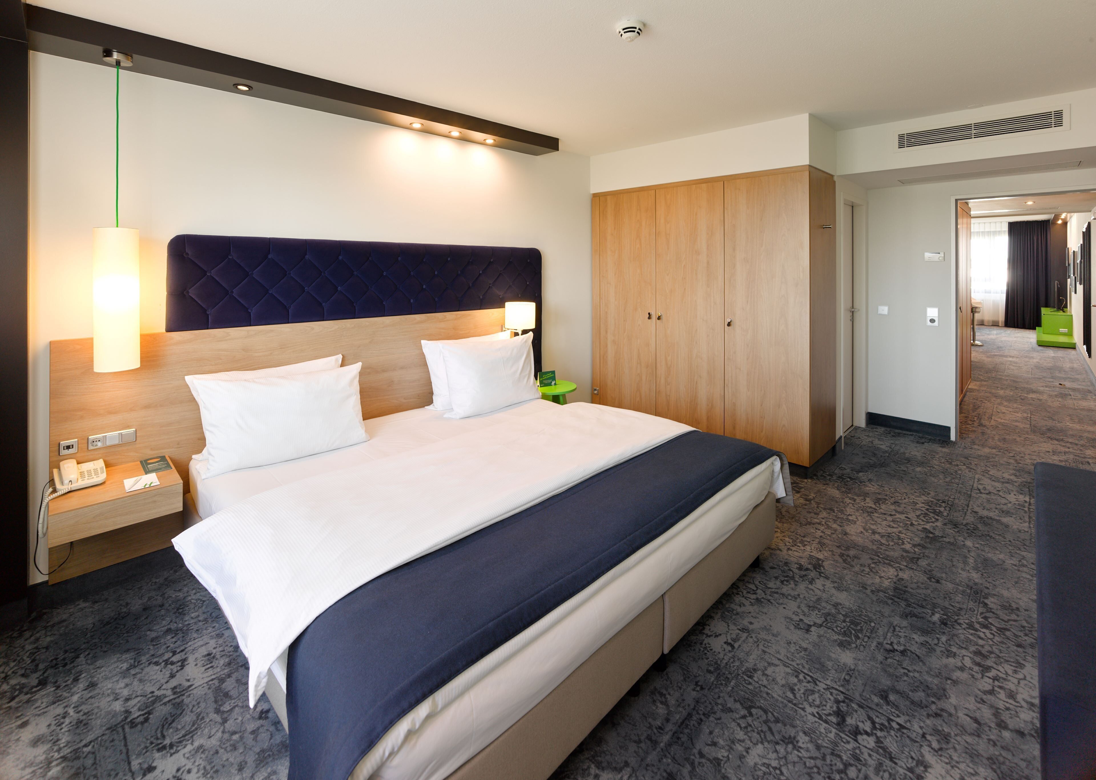 A hotel room with a large bed, a wooden headboard, a bedside lamp, a phone, and a wardrobe.