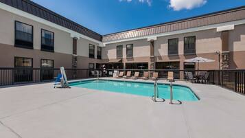 A pool area with a clear blue pool, lounge chairs, and umbrellas.
