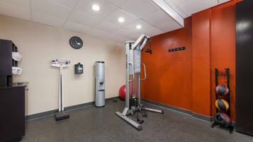 A gym with exercise equipment, a scale, a clock, and a wall-mounted rack with balls.