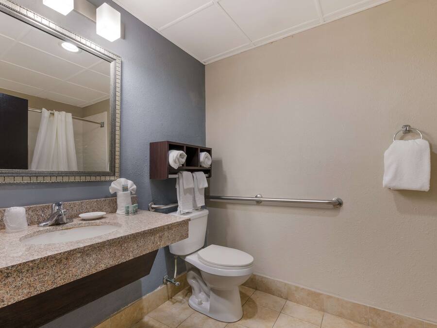 A bathroom with a granite countertop, a white toilet, a towel rack, and a mirror.