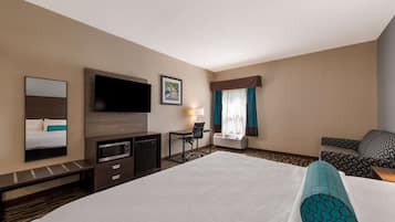 Una habitación de hotel con una cama grande, un escritorio con silla, un televisor de pantalla plana, un microondas y una ventana con cortinas.