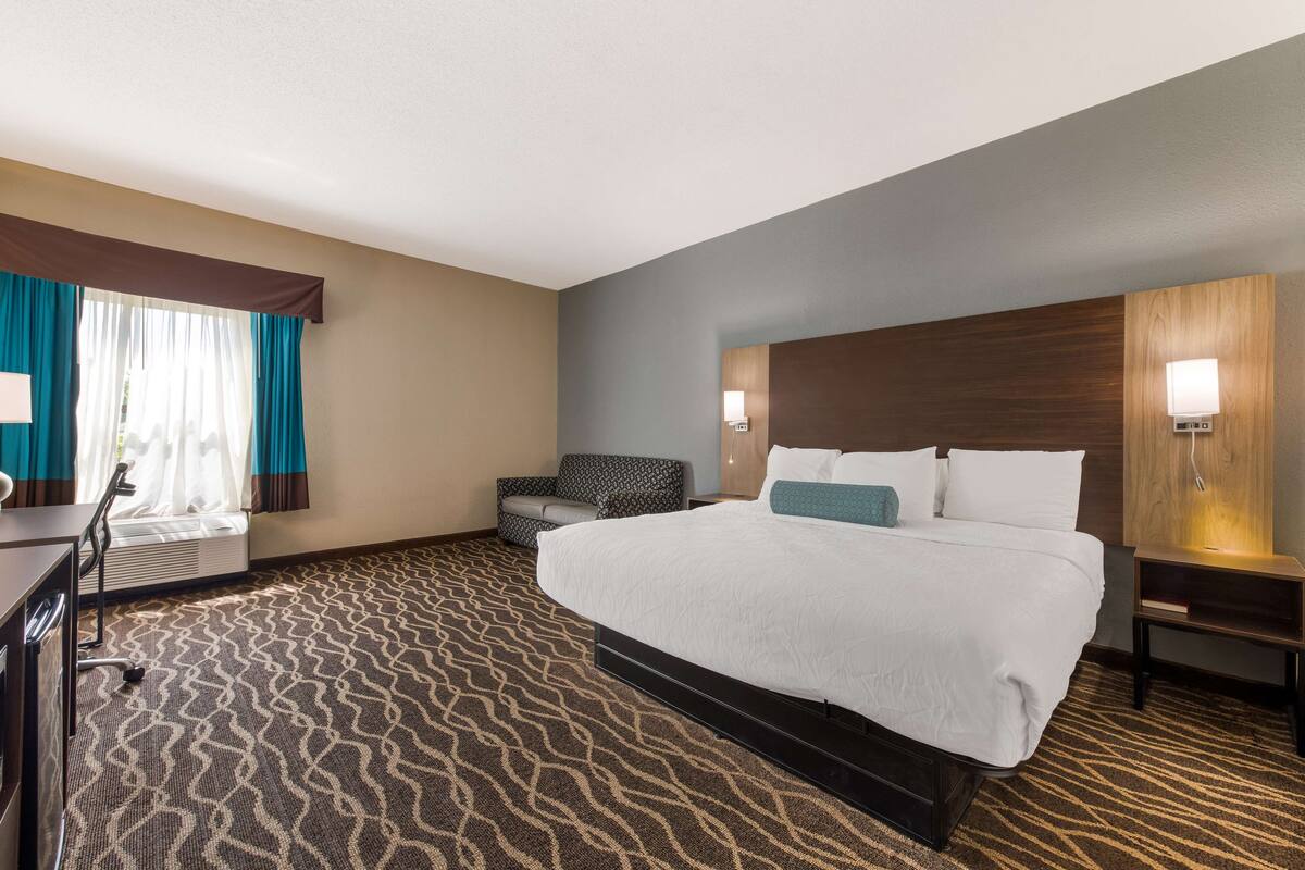 A hotel room with a large bed, a desk, a chair, and a window with curtains.