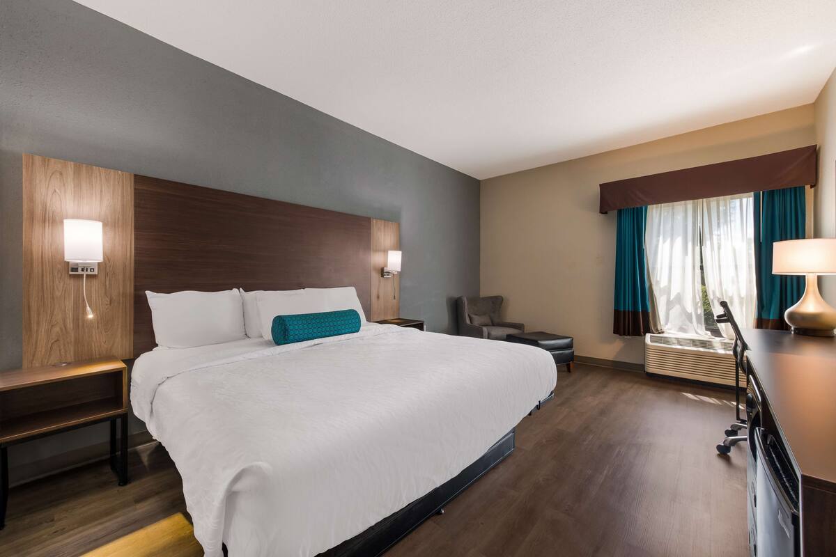 A hotel room with a large bed, bedside tables, a desk, a chair, and a window with curtains.