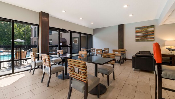 A modern indoor dining area with tables and chairs, large windows, and a view of a swimming pool. - Best Western Albemarle Inn (Albemarle)