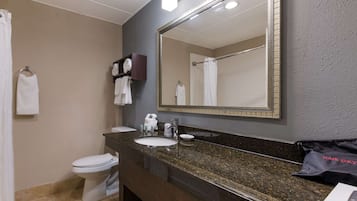 A bathroom with a white toilet, a sink with a dark granite countertop, a large mirror, and a towel rack with white towels.