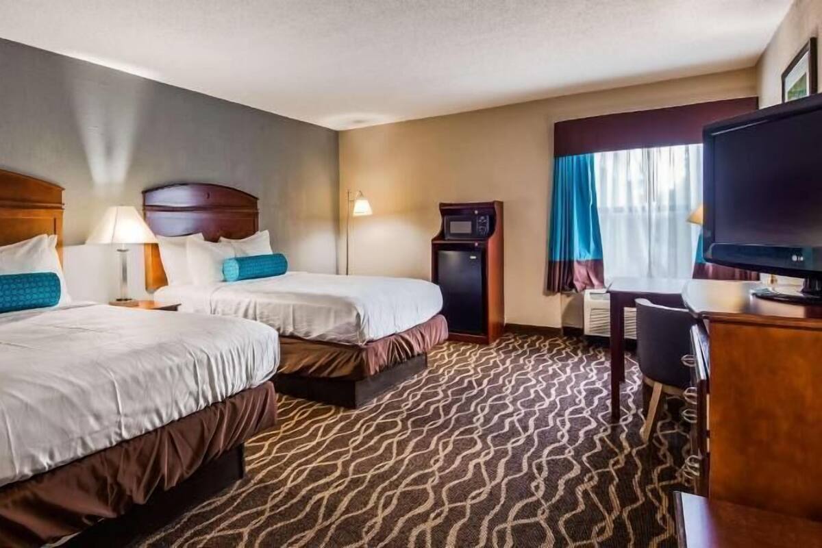 A hotel room with two beds, a desk, a television, a minibar, and a patterned carpet.