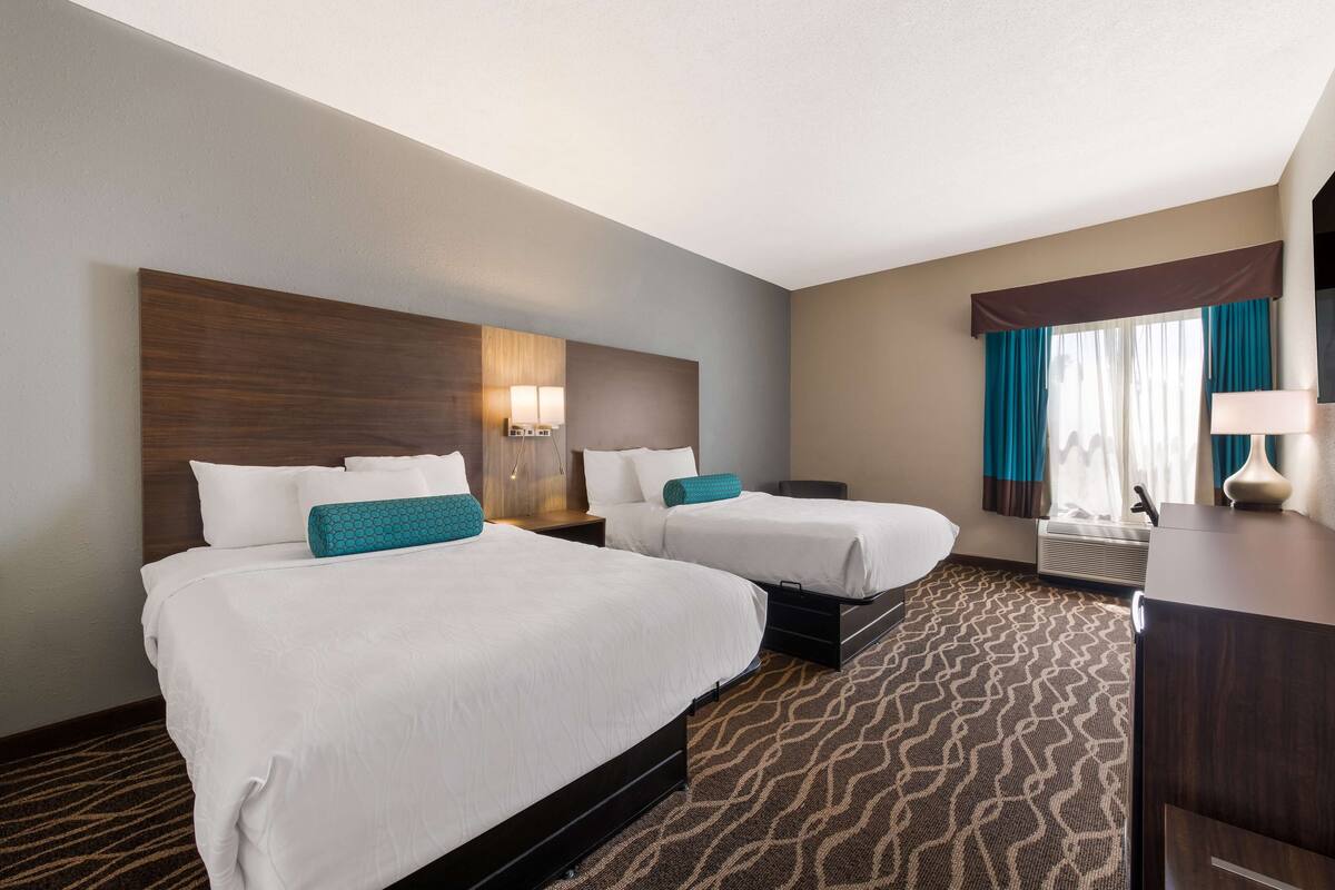 A hotel room with two beds, a desk, and a large window with curtains.