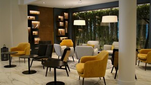 A modern lobby with a marble floor, yellow and grey chairs, and a large window with greenery outside. - Hôtel l'Amirauté (Brest)