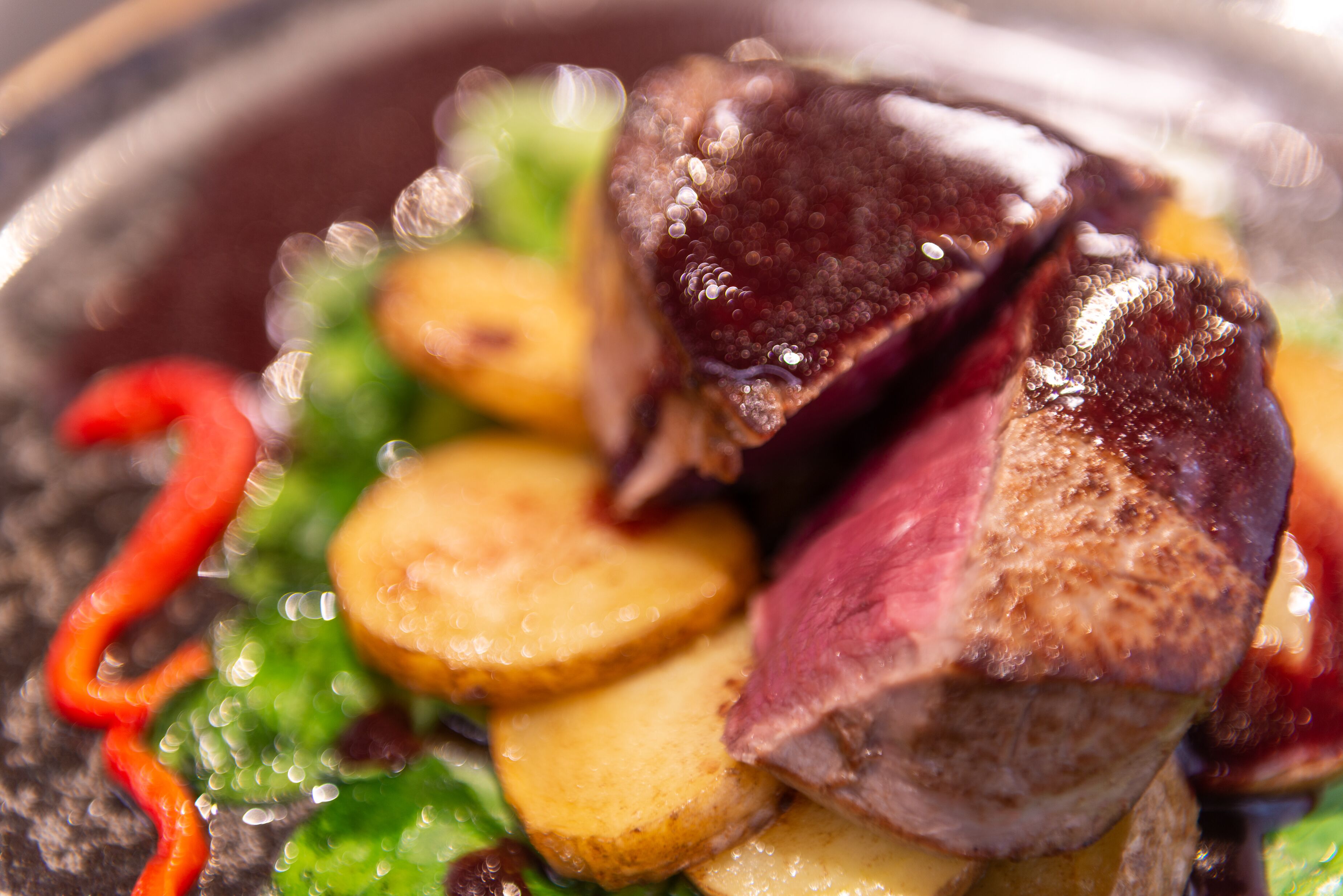 A close-up of a dish with sliced potatoes, a piece of meat, and a red pepper.