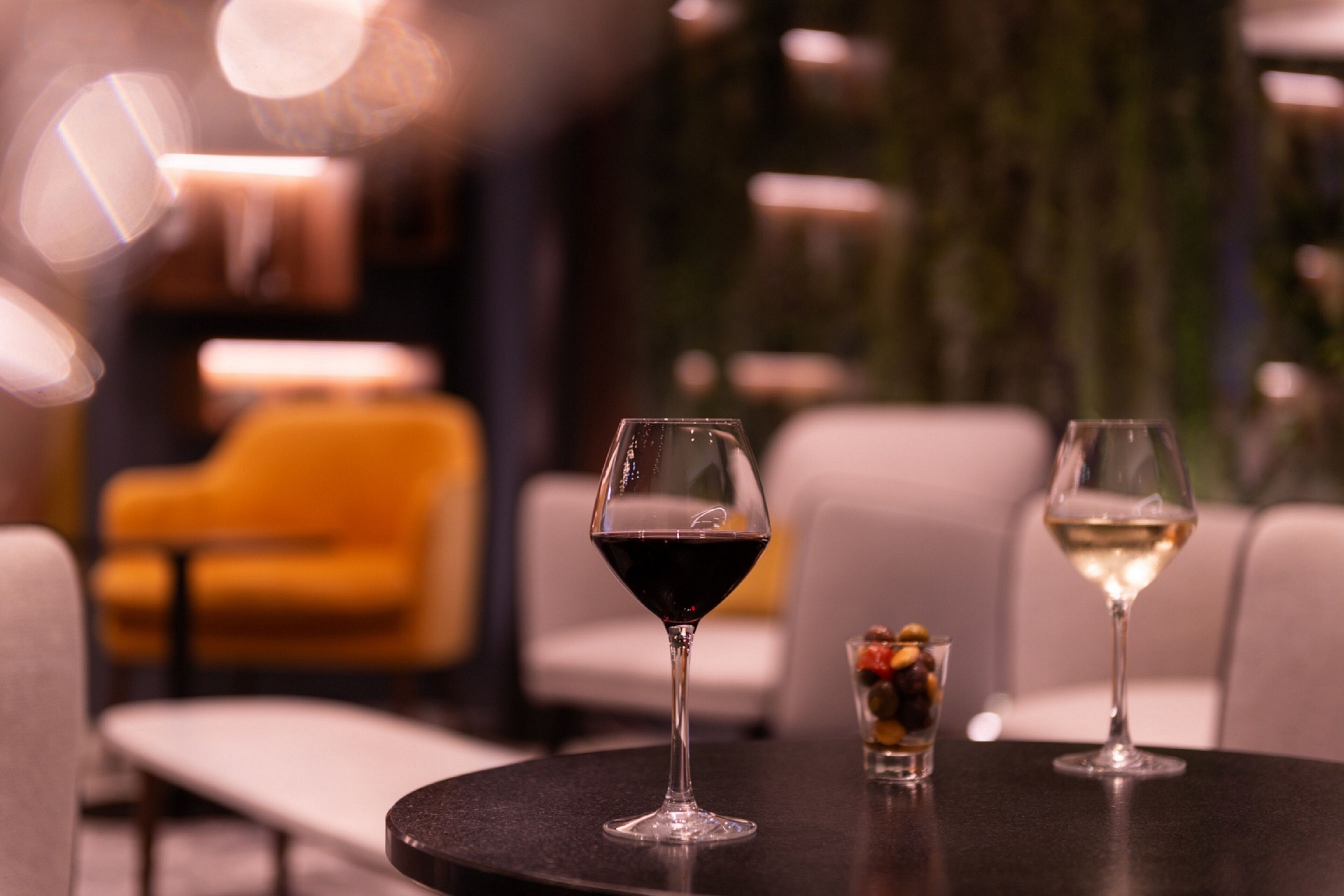 A table with two wine glasses, one with red wine and the other with white wine, and a small glass with olives and nuts.