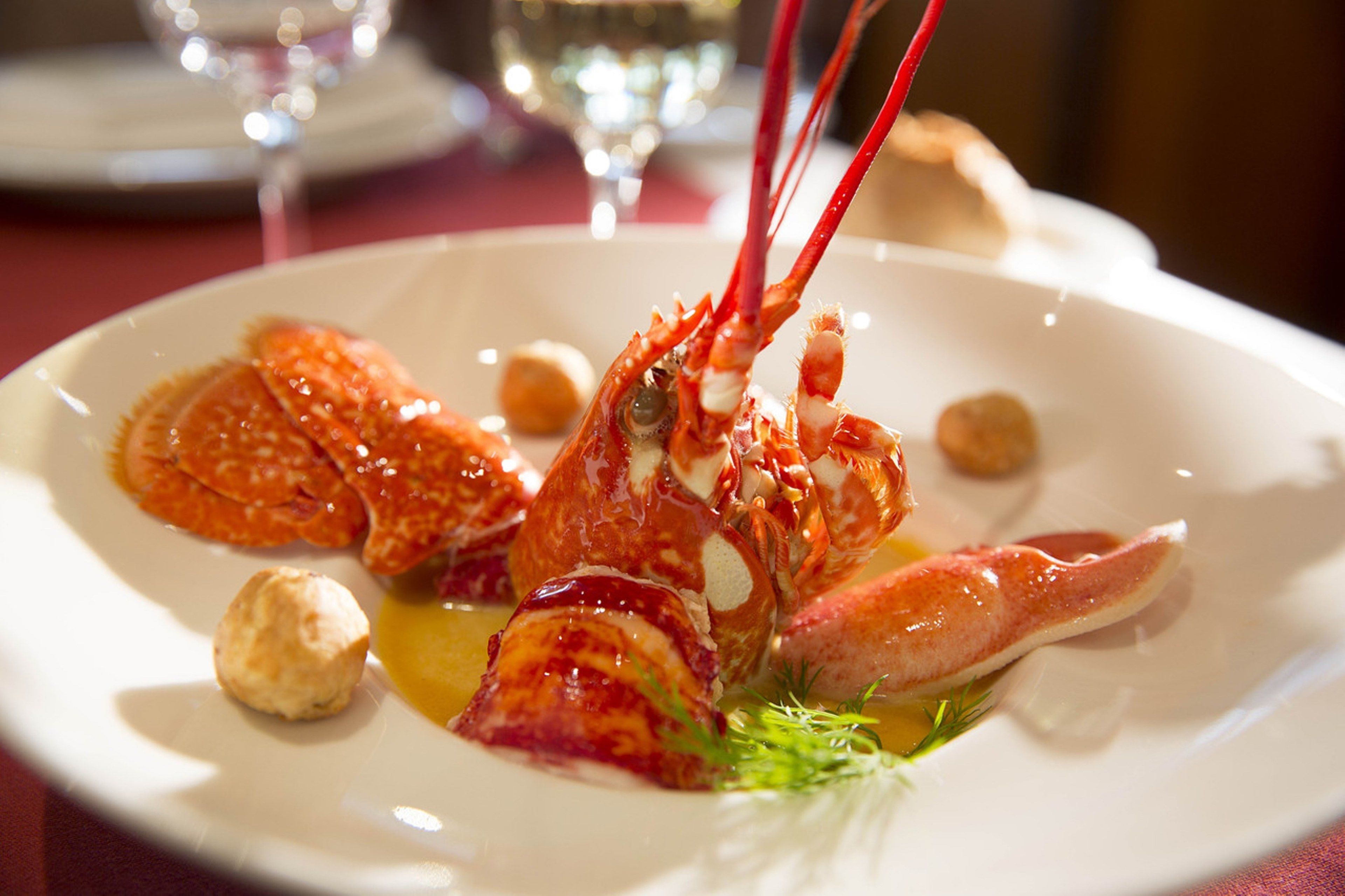 A lobster dish on a white plate with a garnish, accompanied by a glass of water and a bread roll in the background.