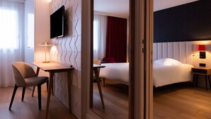 A hotel room with a bed, a desk, a chair, a TV mounted on the wall, and a bedside table with a lamp. - Hôtel l'Amirauté (Brest)