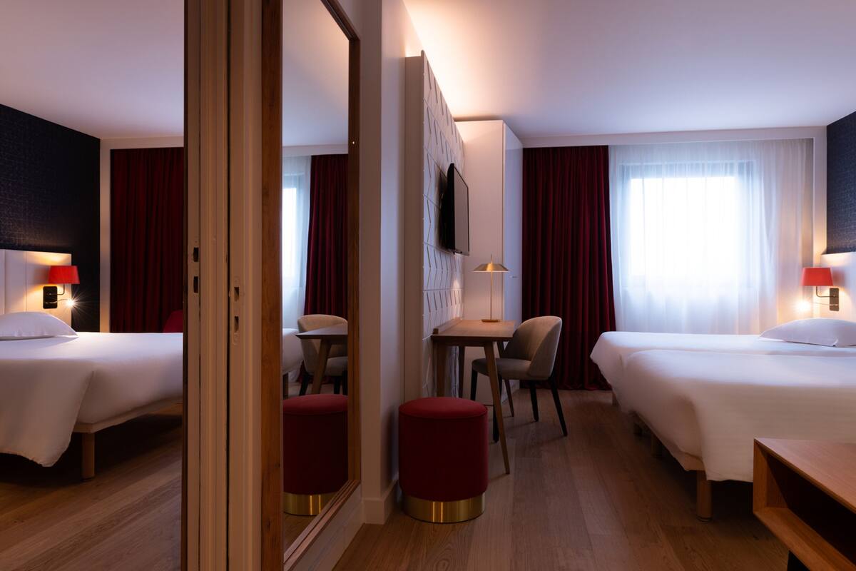 A hotel room with two beds, a desk, a chair, and a TV.