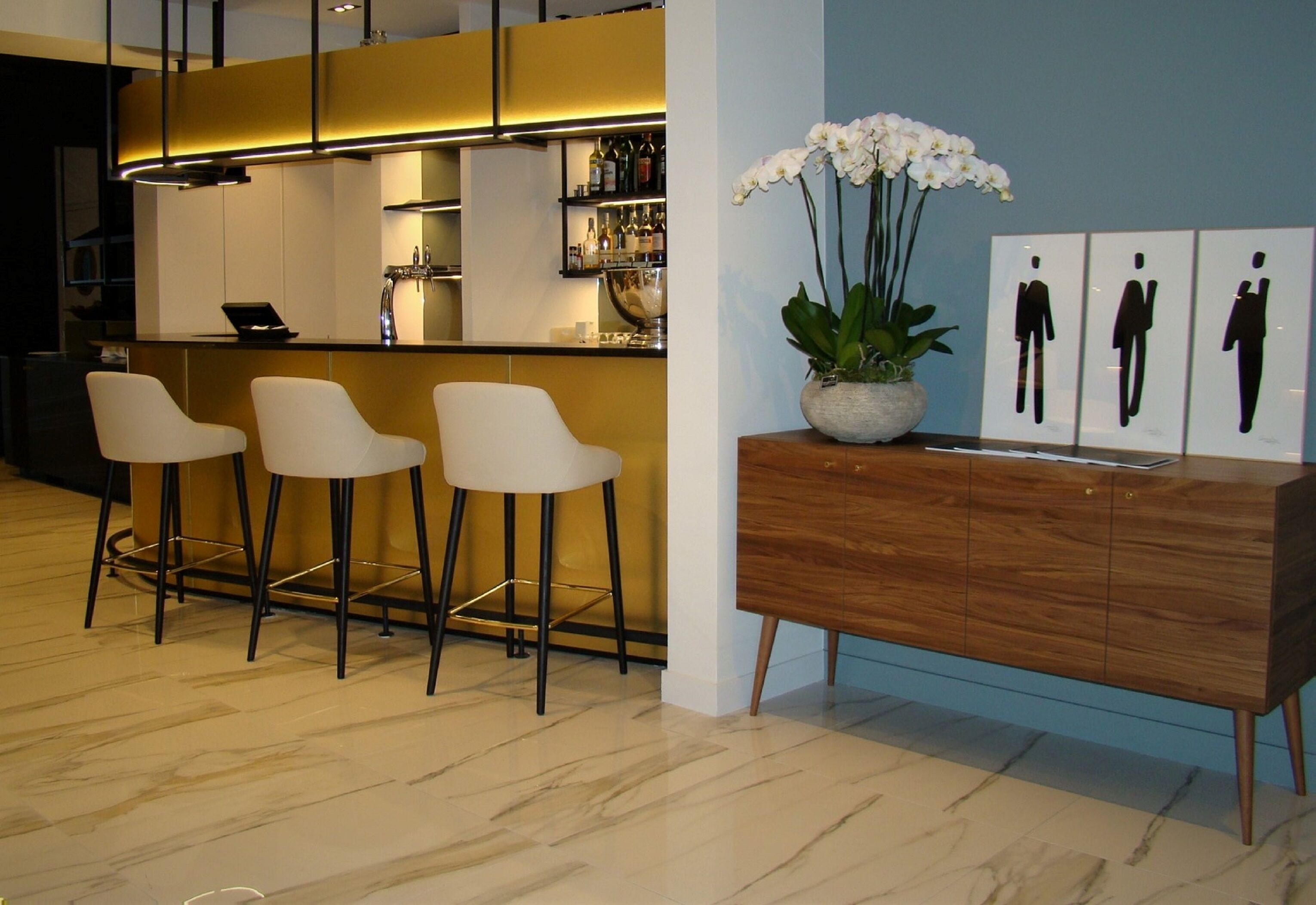 A modern bar area with three bar stools, a wooden cabinet, and a potted orchid.