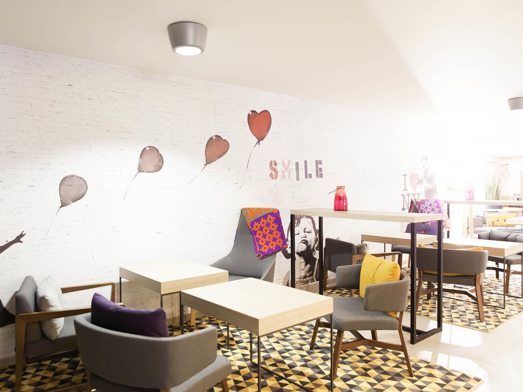 A modern lounge area with a white brick wall, several seating options including a sofa and chairs, a table, and a patterned floor.