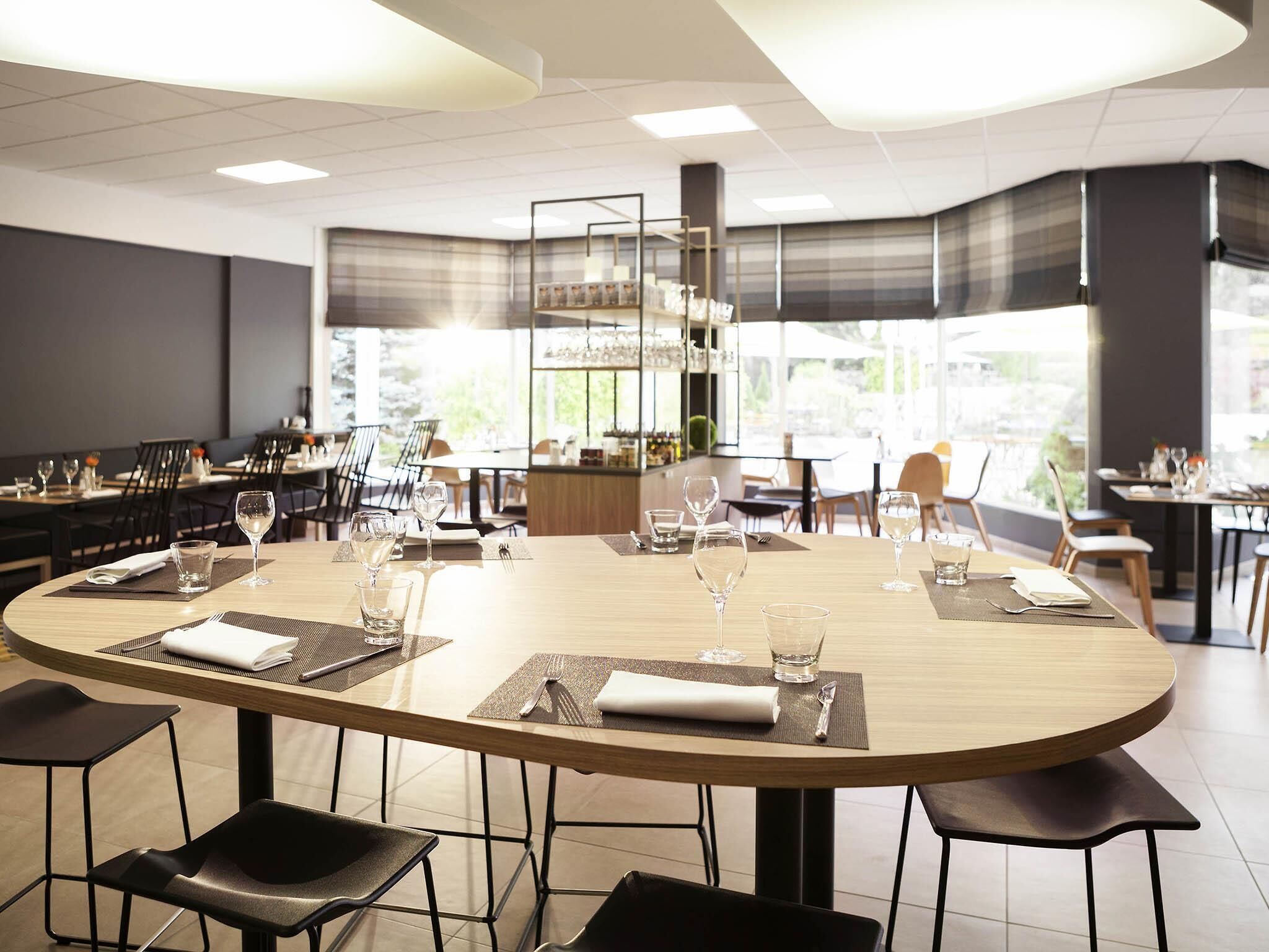 Een restaurant met ronde tafels, zwarte stoelen en een bar.