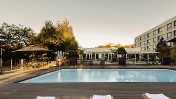 A swimming pool with lounge chairs and umbrellas, surrounded by trees and a building.
