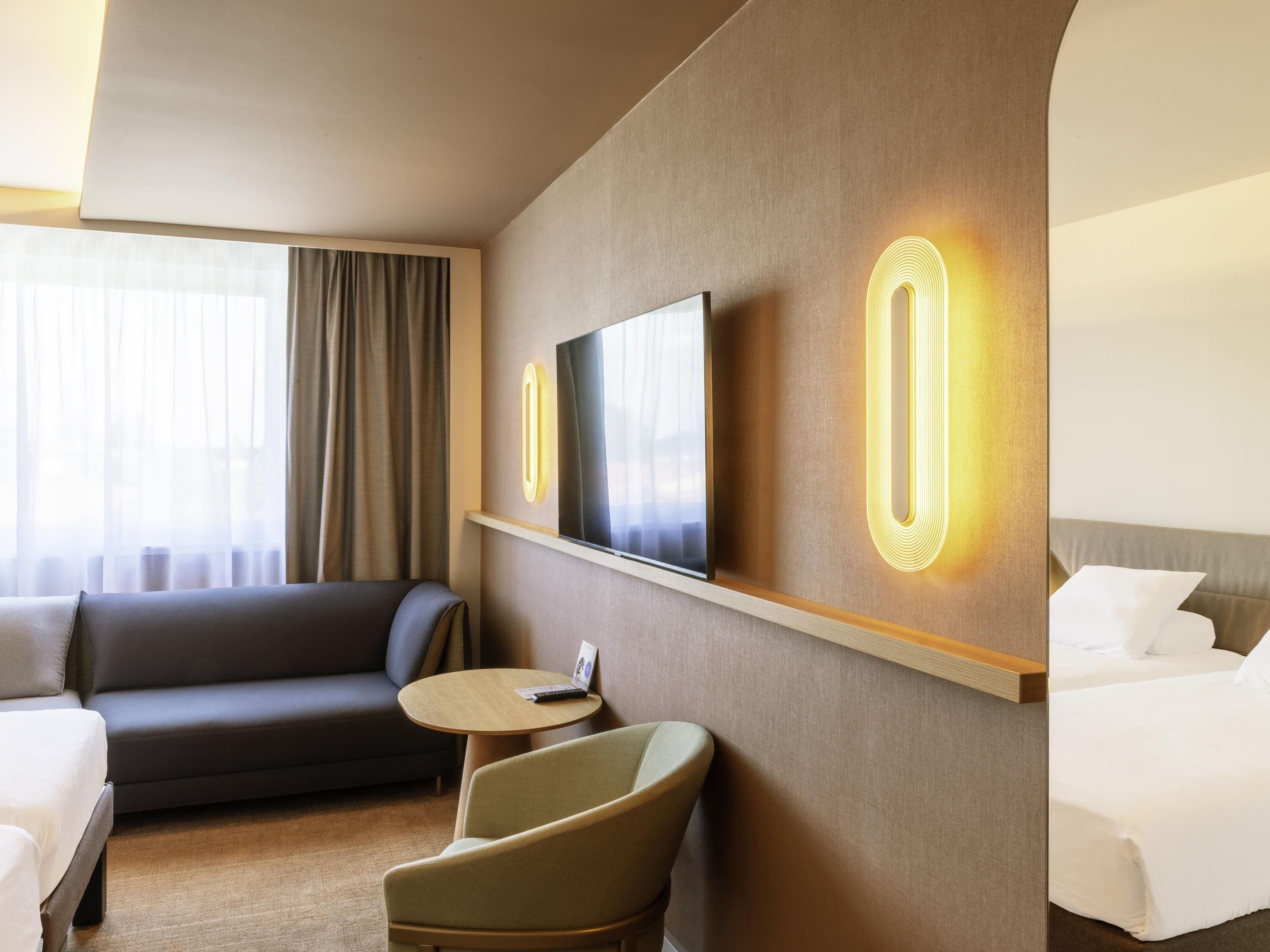 Une chambre d’hôtel avec un canapé, un fauteuil, un lit, une télévision et une petite table.