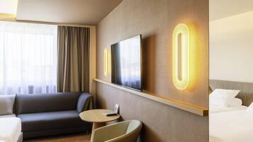 Une chambre d’hôtel avec un canapé, un fauteuil, un lit, une télévision et une petite table.