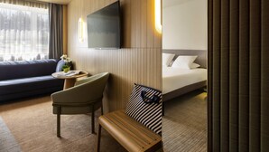 A hotel room with a sofa, a desk with a chair, a bed, and a TV mounted on the wall. - Novotel Nancy (Laxou)