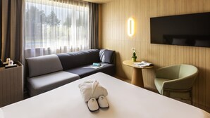 A hotel room with a large bed, a sofa, a small round table, a TV, and a chair. - Novotel Nancy (Laxou)