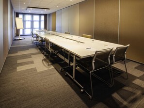 A conference room with a long table, chairs, and a projector screen. - Novotel Nancy (Laxou)
