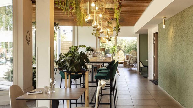 A modern dining area with a wooden ceiling, hanging light fixtures, and a view of the outdoors. - Novotel Nancy (Laxou)